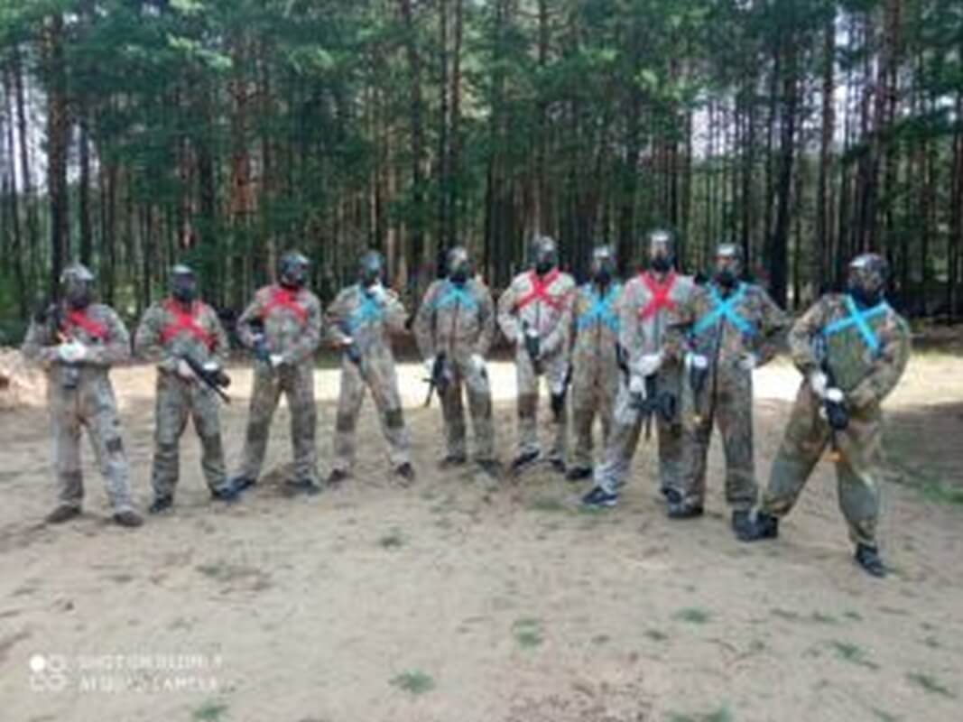 Grupa osób w pełnym wyposażeniu do paintballa w lesie, potencjalni gracze poszukujący informacji o cenach paintballa w Białymstoku.