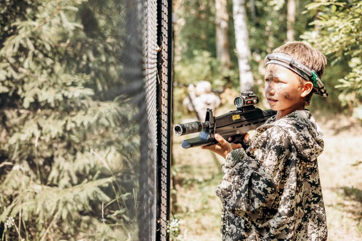 Dziecko w kamuflażowym stroju grające w paintball podczas urodzin w lesie.