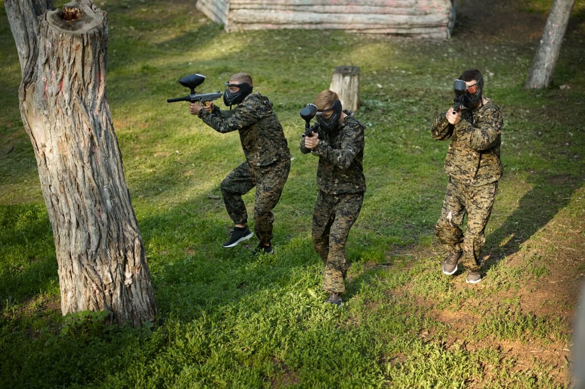 Trzy osoby grające w paintball dla firm na otwartym terenie.
