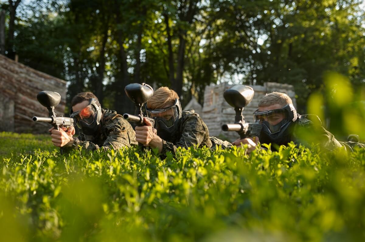 Grupa mężczyzn w maskach ochronnych gra w paintball dla grup zorganizowanych Białystok na świeżym powietrzu.