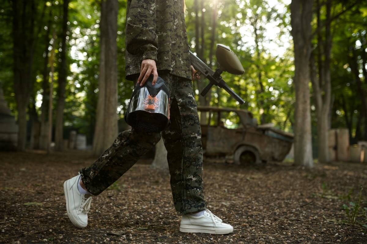 Osoba w stroju moro, trzymająca maskę i marker, prezentuje paintball poradnik dla początkujących.