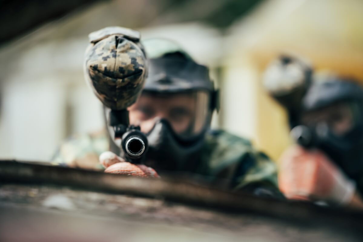 Gracze w maskach i mundurach mierzą do celu, uczestnicząc w paintball scenariusze grup zorganizowanych.