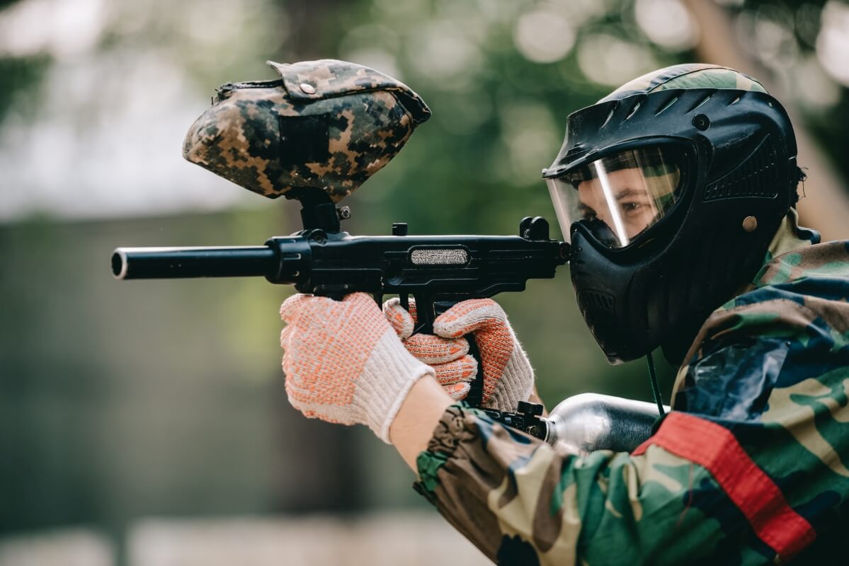 Dziecko w masce ochronnej celuje markerem do paintballa, podkreślając bezpieczeństwo paintball dzieci.