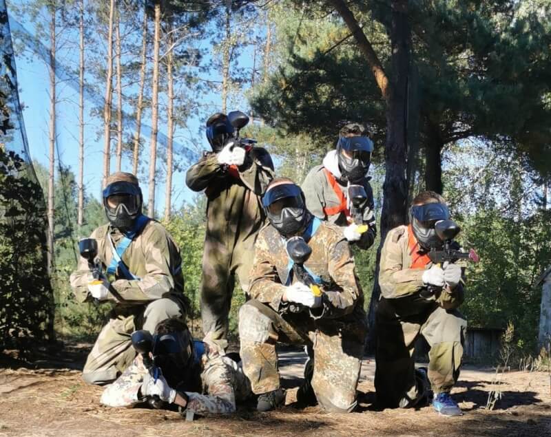 Grupa przyjaciół w lesie, ubrana w stroje paintballowe, tworzy historie paintball wieczór kawalerski na świeżym powietrzu.
