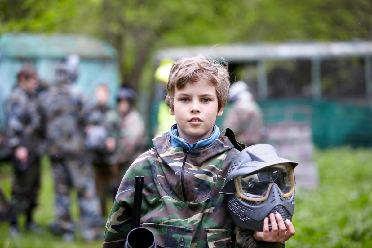 Dziecko w stroju do paintballa, trzymające maskę, co podkreśla znaczenie tematu: bezpieczeństwo paintball dzieci.