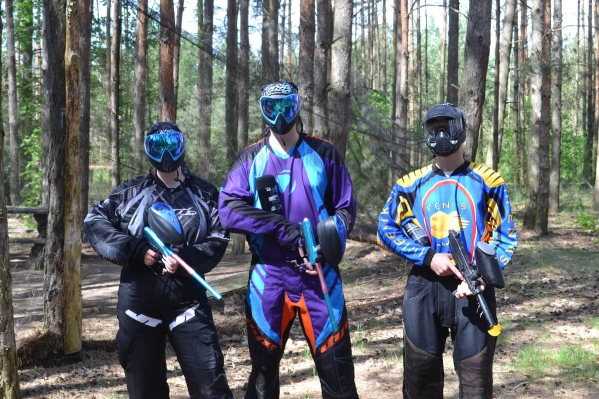 Trzy osoby w sprzęcie do paintballu w lesie pokazują korzyści paintball grupy zorganizowanej.