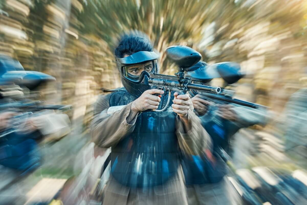 Osoba w masce celuje markerem, podkreślając korzyści paintball firmy, takie jak integracja i współpraca zespołowa.