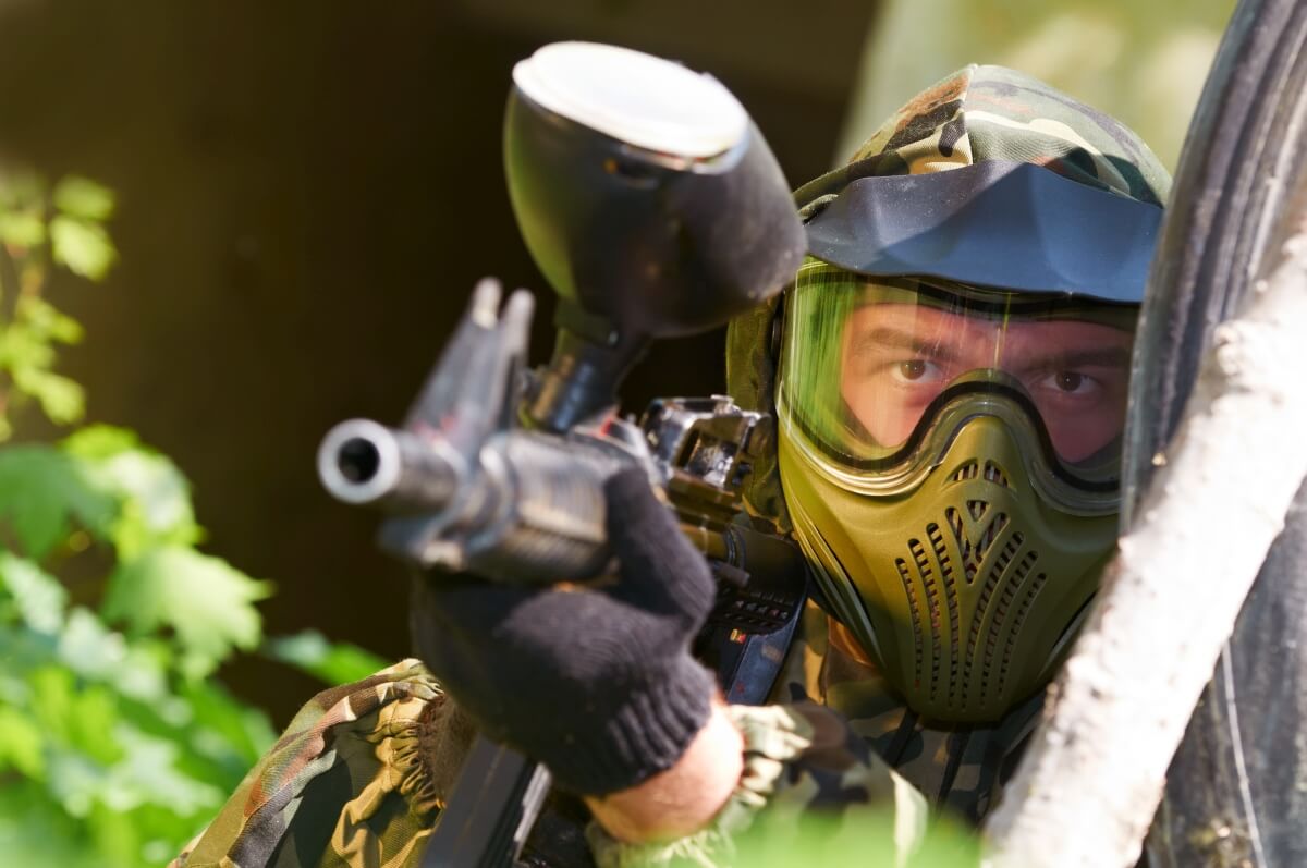 Osoba w masce celuje z karabinku paintballowego, co idealnie pasuje do organizacja wieczoru kawalerskiego paintball.